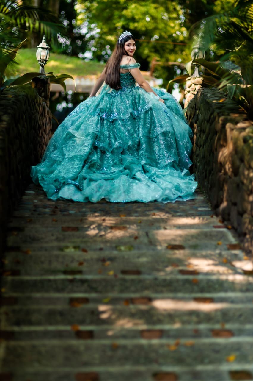 Quinceañera in a teal ballgown crossing the garden at her party